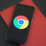 Close-up of a smartphone with Chrome browser logo on screen placed on a red notebook.